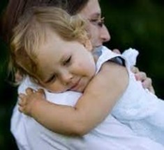 A woman, Erica Barnes, with dark hair and glasses wearing a white shirt holding a young girl, Chloe Barnes, in a white sundress