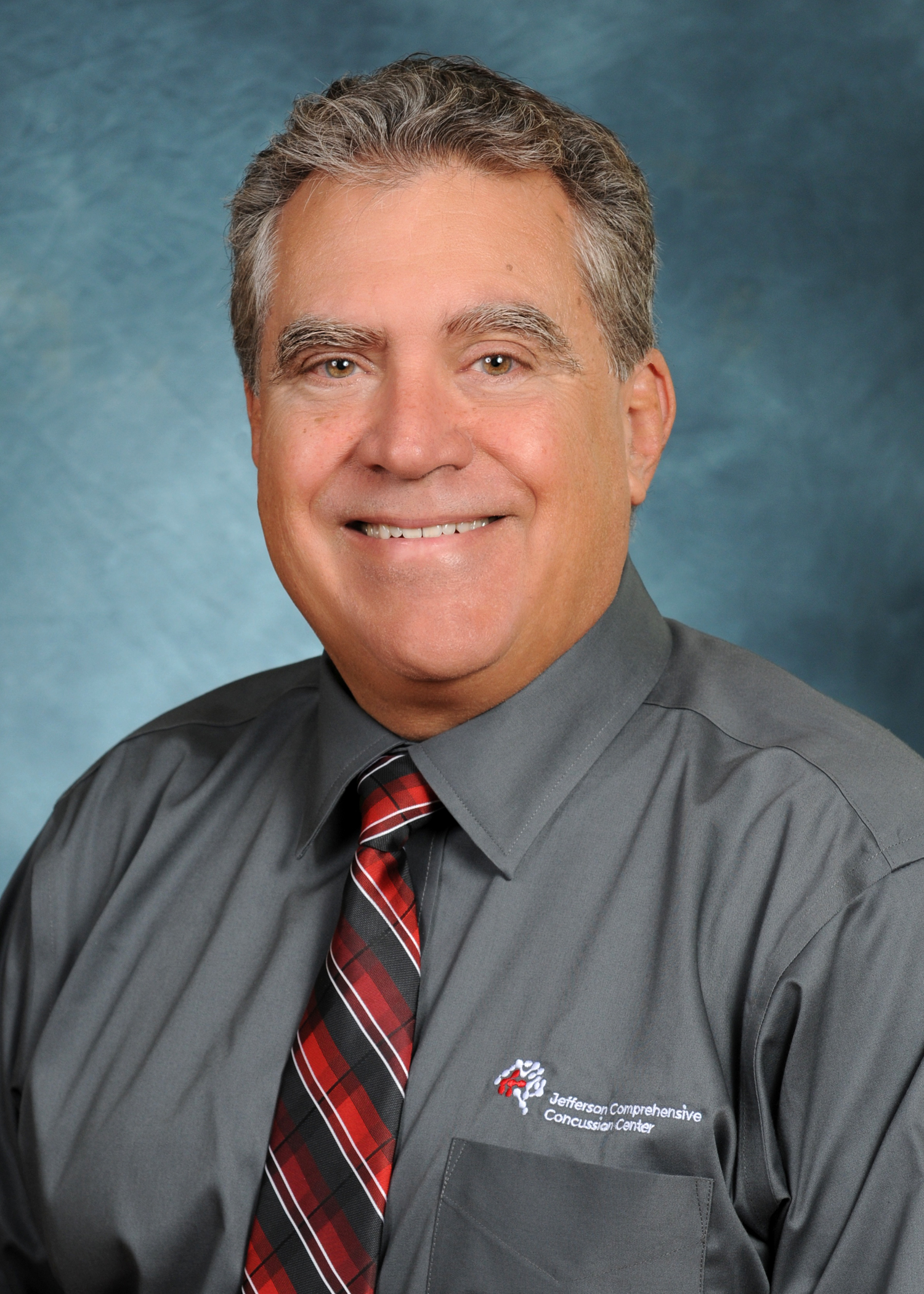 Dr Scott Edmonds wearing a grey button down shirt with a black red and white tie