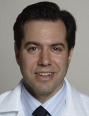 Dr. Matthew Galsky wearing a blue striped collared shirt and a dark tie with a white coat