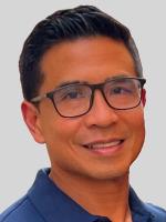 Elmo Agatep, MD, is a board-certified family medicine physician with a certified added qualification (CAQ) in sports medicine. Dr. Agatep is smiling at the camera. He has short black hair and is wearing black rimmed glasses and a blue collared shirt. 