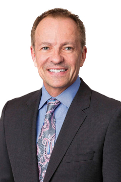 Dr. Bradley Monk wearing a blue collared shirt, grey suit jacket and a paisley tie