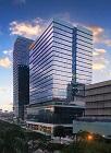 This image is of the the Optum office building located in Makati, PH. It is a tall office building with mirrored windows and the background is a blue sky with white clouds.