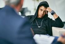 Black male adolescent listening to his counsellor during therapy session at therapist's.